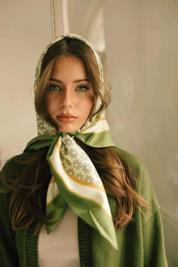 Woman wearing a stylish green headscarf with floral patterns and green cardigan, indoors.