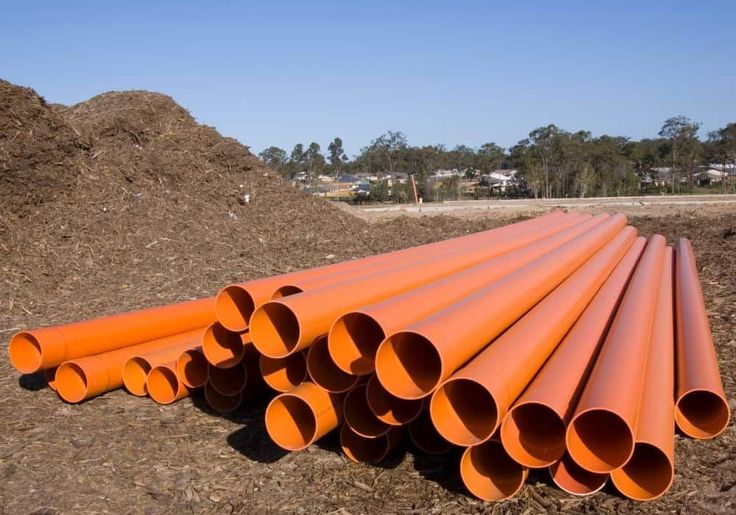 Stack of large orange pipes on construction site with mulch piles in background.