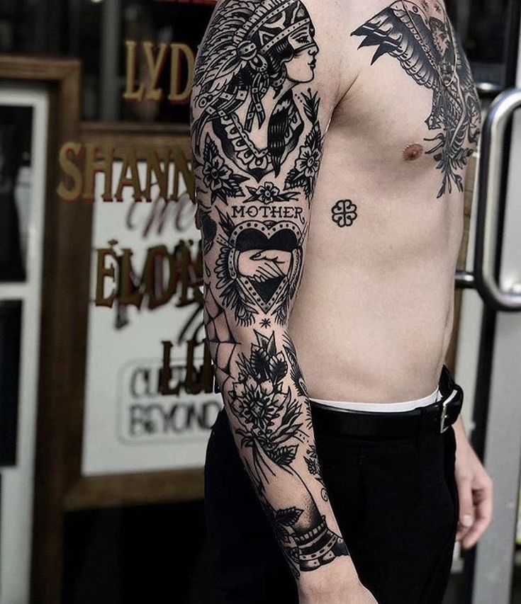 Man with intricate black tattoo sleeve featuring traditional designs, tribal art, and Mother text on arm.