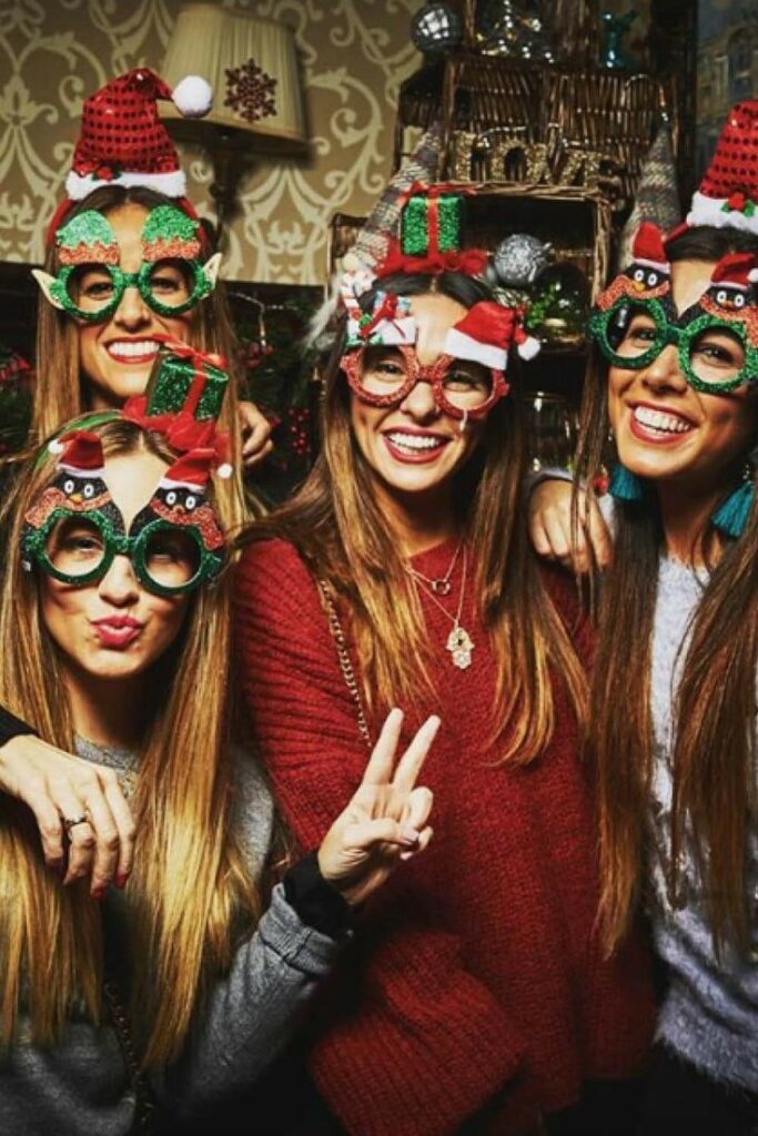 Four people in festive glasses and sweaters celebrating at a Christmas party, smiling and having fun.