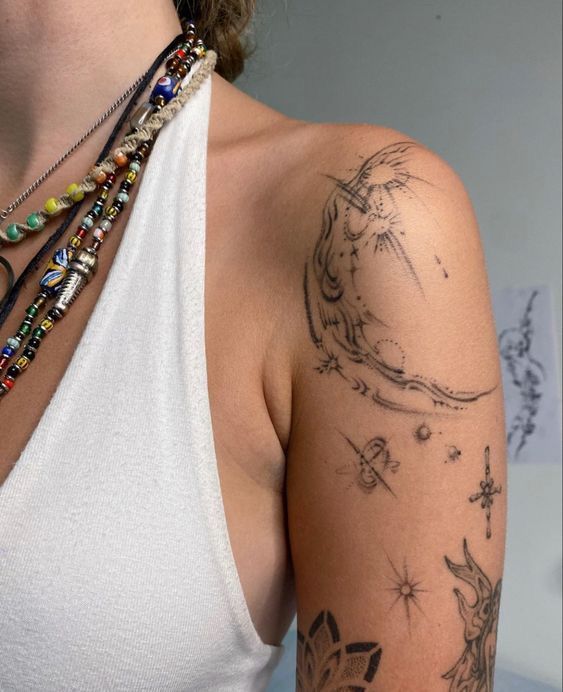 Arm with celestial tattoos and colorful bead necklaces, wearing a white tank top.