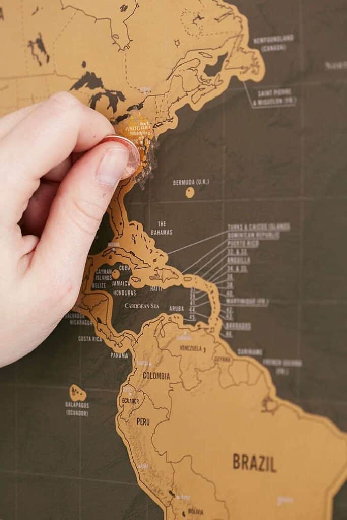 Hand scratching off USA on a scratch-off world map, revealing travel destinations.