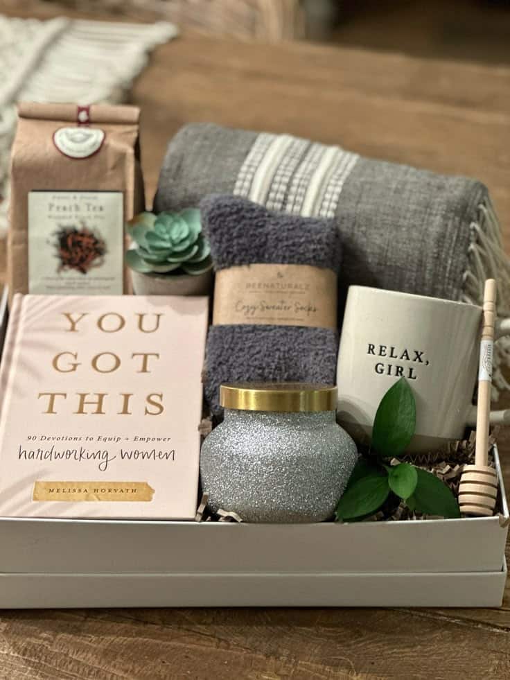 Gift box with a book, tea, succulent, blanket, candle, socks, and mug; perfect for relaxation and self-care.