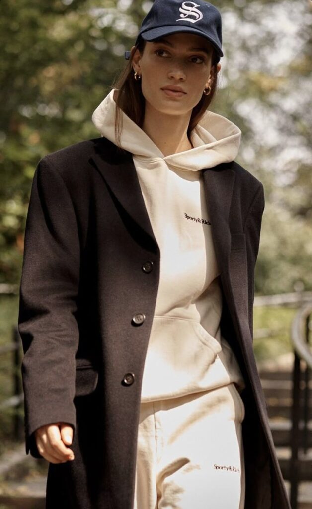 Woman in stylish streetwear: black coat, beige hoodie, blue cap. Urban fashion.