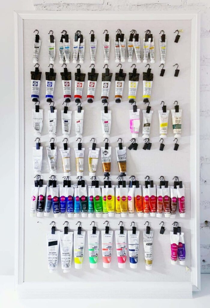 Wall display of assorted paint tubes organized by color for creative studio inspiration.