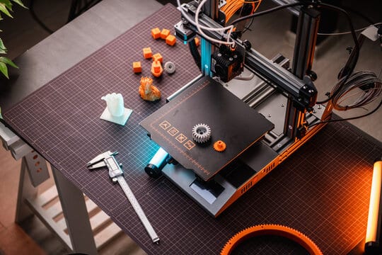 3D printer on workbench with calibration tools and printed items, including gears and a small sculpture.