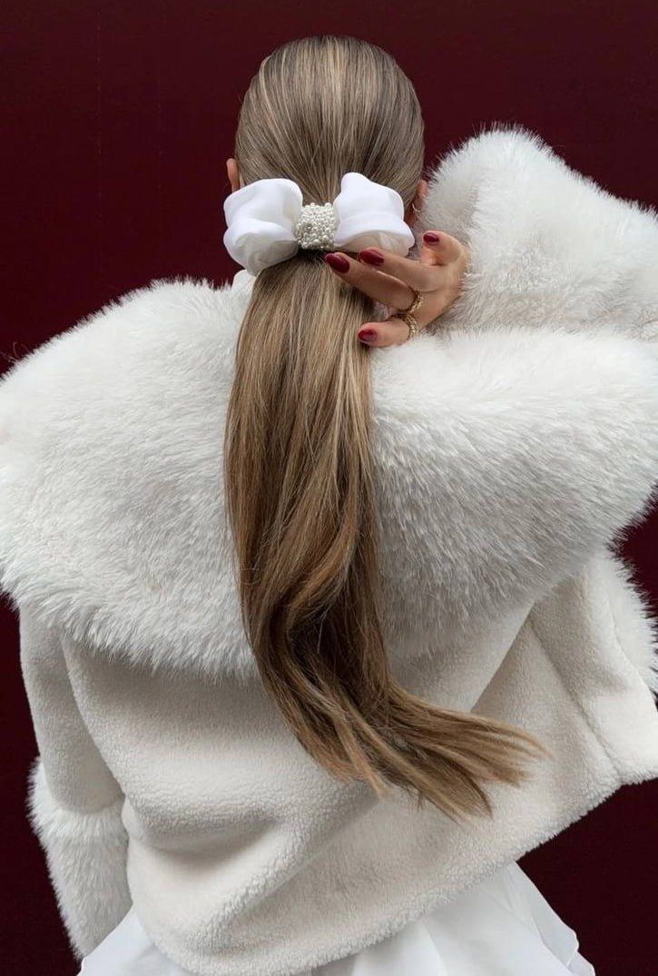 Woman with long hair in a white fur coat, adorned with a decorative hair bow.