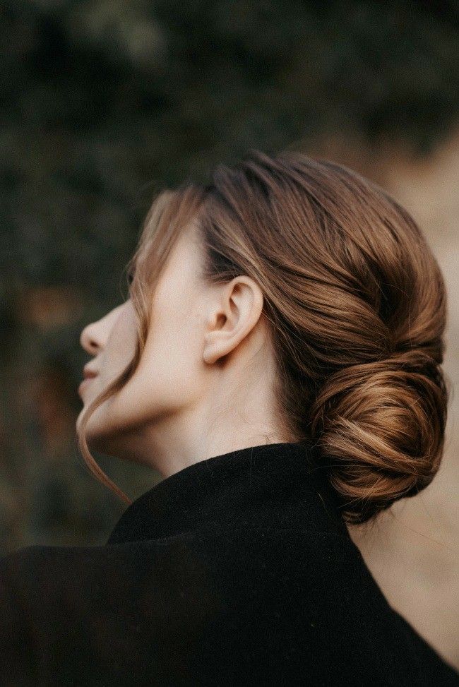 Woman with elegant bun hairstyle, side profile; blurred nature background.