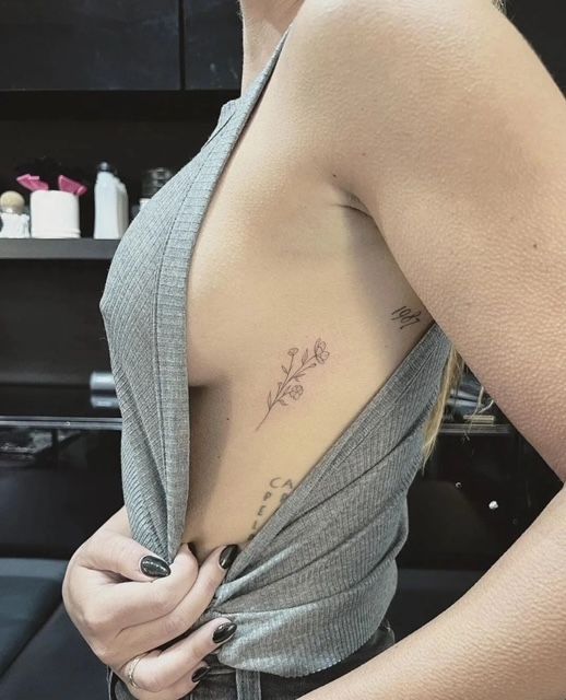 3a72140a0ab23d1cd075eef7fdb15052 Side tattoo of delicate flowers on person's ribcage, shown with a gray top in a modern setting. | Sky Rye Design Side tattoo of delicate flowers on person's ribcage, shown with a gray top in a modern setting.