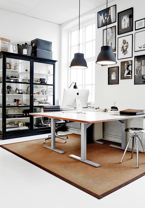 Modern office with a sleek desk, computer, stylish shelves, and wall art, illuminated by hanging lights.