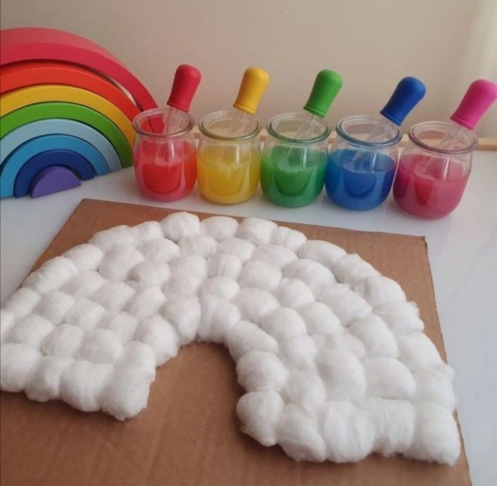 _ 4 Rainbow craft setup with cotton balls and jars of paint in rainbow colors on a table. | Sky Rye Design Rainbow craft setup with cotton balls and jars of paint in rainbow colors on a table.