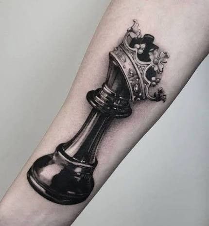 _ 4 Tattoo of a chess piece with a crown on forearm, symbolizing strategy and power in black and gray ink. | Sky Rye Design Tattoo of a chess piece with a crown on forearm, symbolizing strategy and power in black and gray ink.