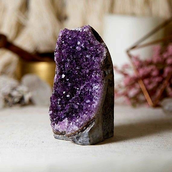 Amethyst crystal standing decoratively on a table, with a blurred background featuring soft, earthy tones.