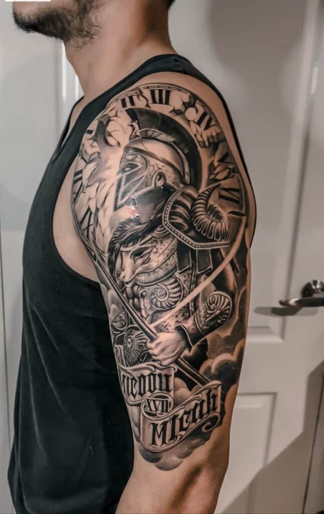 Detailed Spartan warrior tattoo design on a man's upper arm in grayscale.