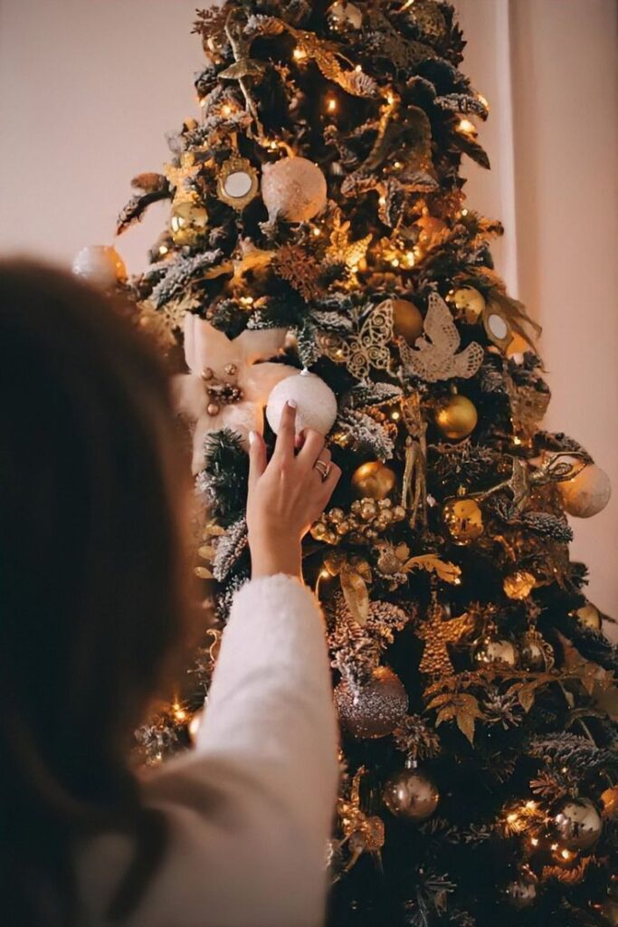 Person decorating a Christmas tree with ornaments and lights, creating a festive holiday atmosphere at home.