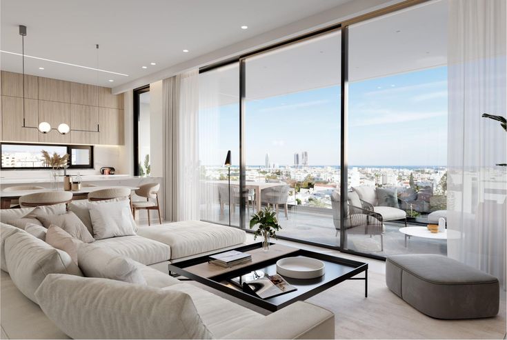 Modern open-plan living room with beige sofa, large glass doors, and balcony view of cityscape and ocean in daylight.