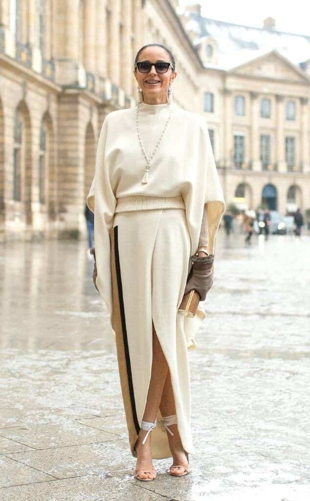 Fashionable woman in chic cream outfit and sunglasses poses on a wet city street.
