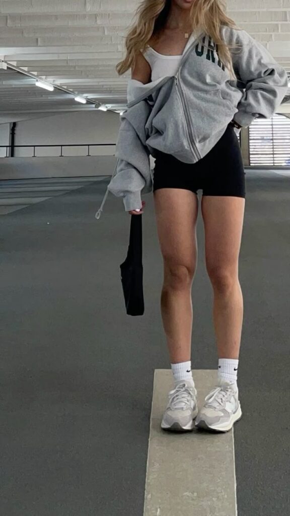 Person in casual outfit with gray hoodie, black shorts, and sneakers standing in a parking garage.