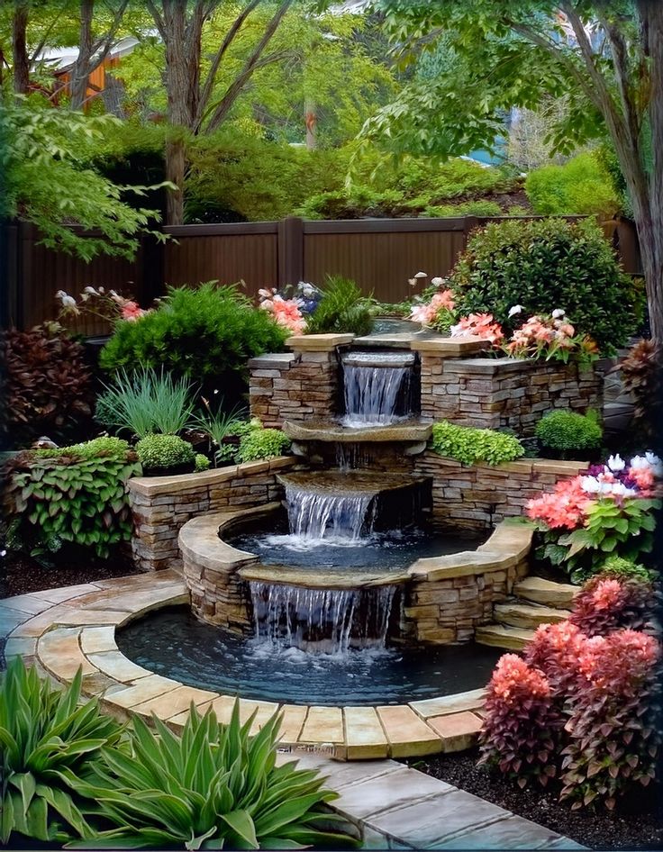 411d23d5-27d9-46a1-8f3a-51bd899c81ab Stone tiered garden waterfall surrounded by lush greenery and colorful flowers. | Sky Rye Design Stone tiered garden waterfall surrounded by lush greenery and colorful flowers.