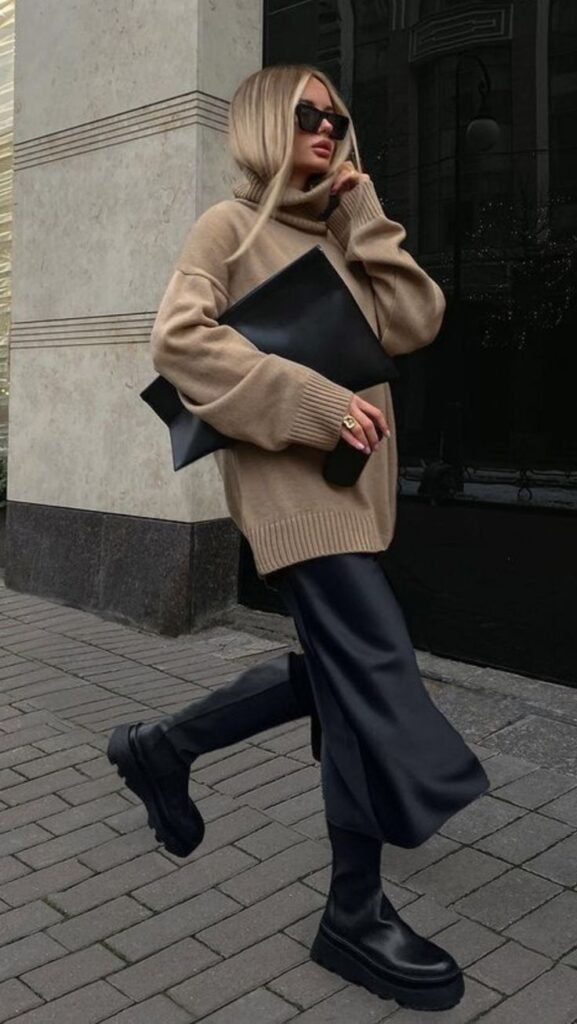 Stylish woman in oversized beige sweater, black pants, and sunglasses holding a large black clutch on city street. Outfit Ideas for Autumn
