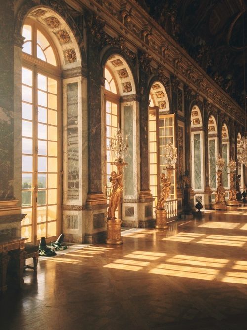 Sunlit hall with ornate golden statues and large arched windows in an elegant palace, creating a majestic ambiance.