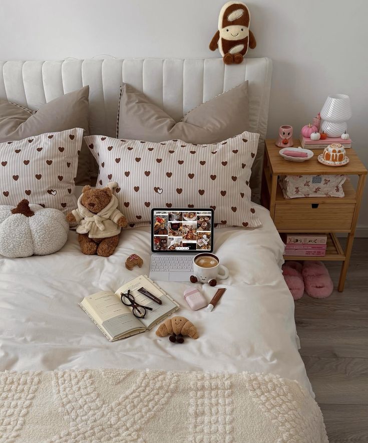 Screenshot Cozy bedroom with heart-pattern pillows, laptop, teddy bear, coffee, and notebook on bed, creating a warm, inviting space. | Sky Rye Design Cozy bedroom with heart-pattern pillows, laptop, teddy bear, coffee, and notebook on bed, creating a warm, inviting space.
