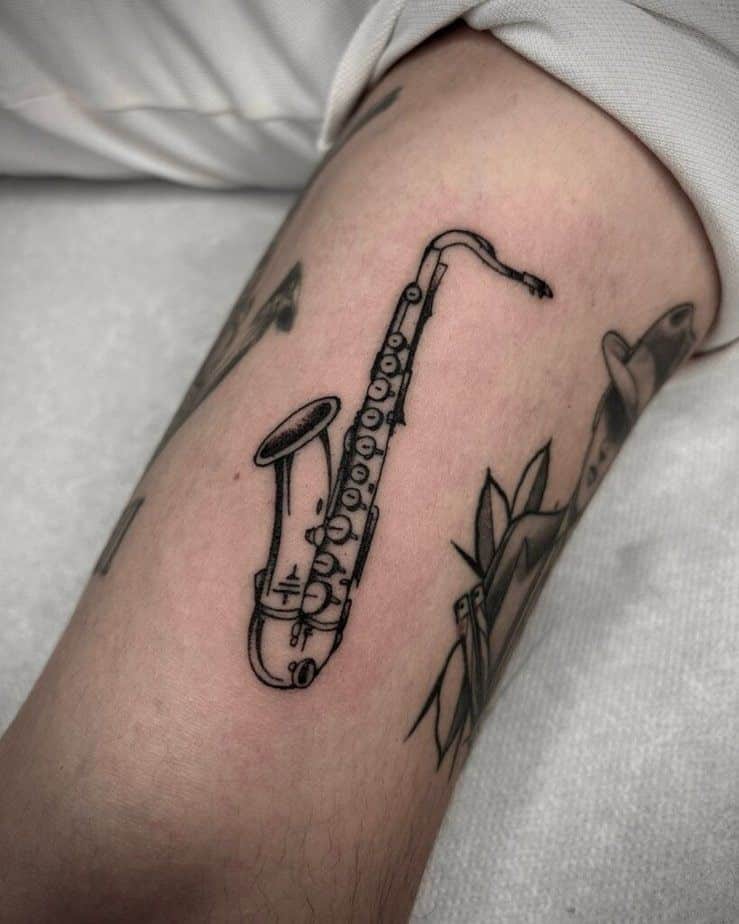 Saxophone tattoo on forearm, black ink design showcasing detailed musical instrument art in a minimalist style.