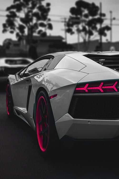 Sleek sports car with vibrant red taillights and rims, parked on street, showcasing modern design and luxury appeal.