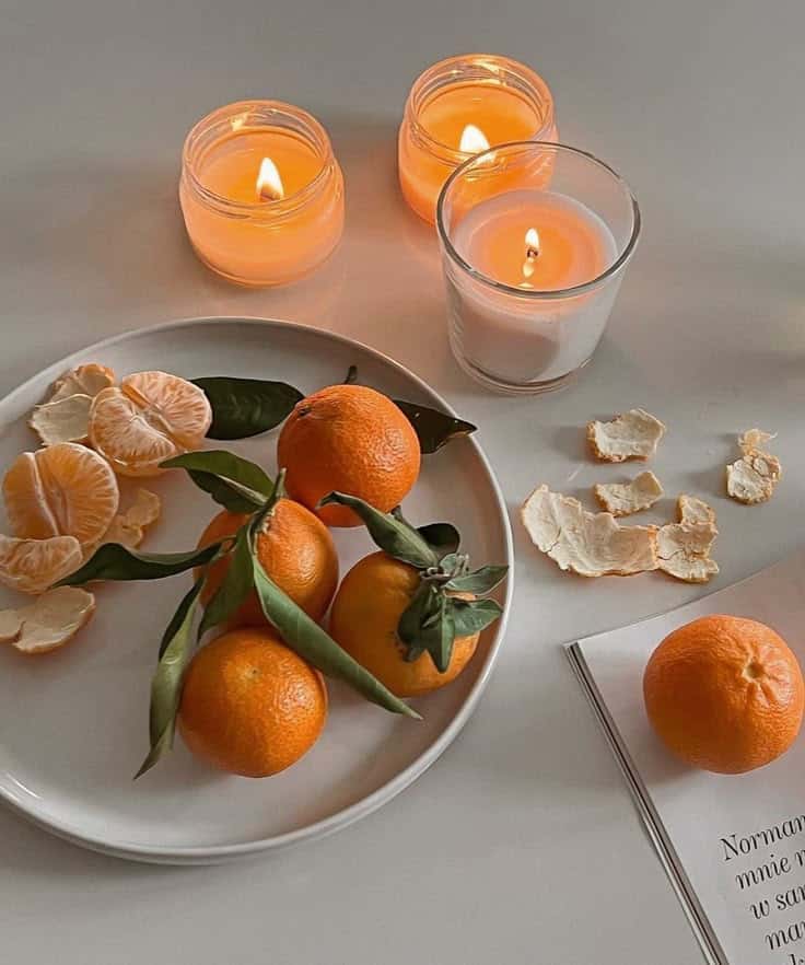 _ 5 Fresh tangerines and peels on a white plate with glowing candles in a cozy setting. | Sky Rye Design Fresh tangerines and peels on a white plate with glowing candles in a cozy setting.
