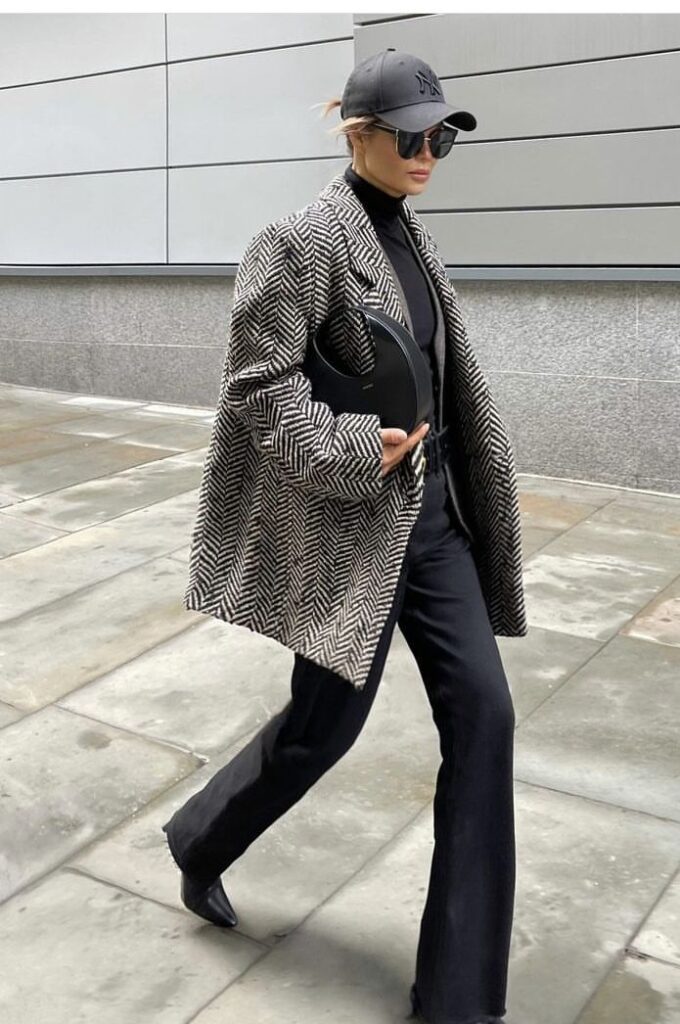 _ 5 Fashionable woman in herringbone coat, black pants, sunglasses, and cap walking on city sidewalk. Stylish urban outfit. | Sky Rye Design Fashionable woman in herringbone coat, black pants, sunglasses, and cap walking on city sidewalk. Stylish urban outfit.