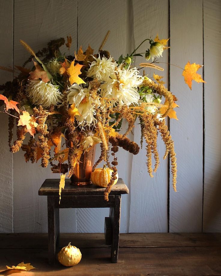 Autumn floral arrangement with orange leaves and gourds on rustic table against wooden background.