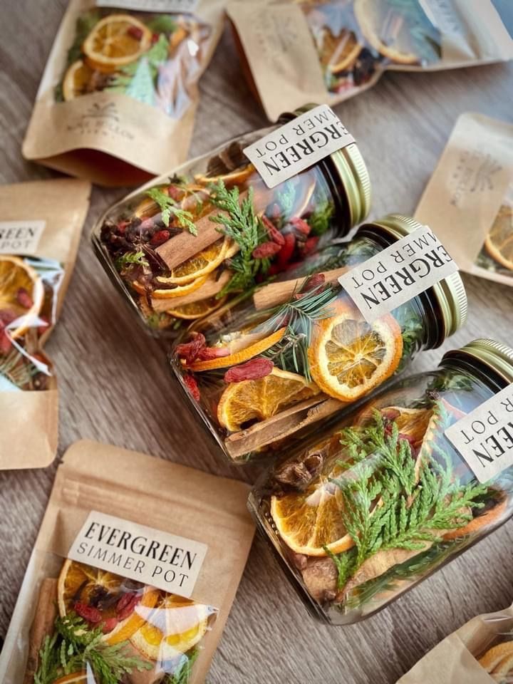 Jars and pouches of Evergreen simmer pots with dried oranges, cinnamon, and greenery on a wooden surface.