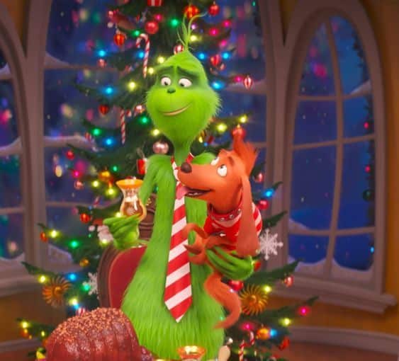 Green character and dog celebrate Christmas by a festive tree with colorful lights.