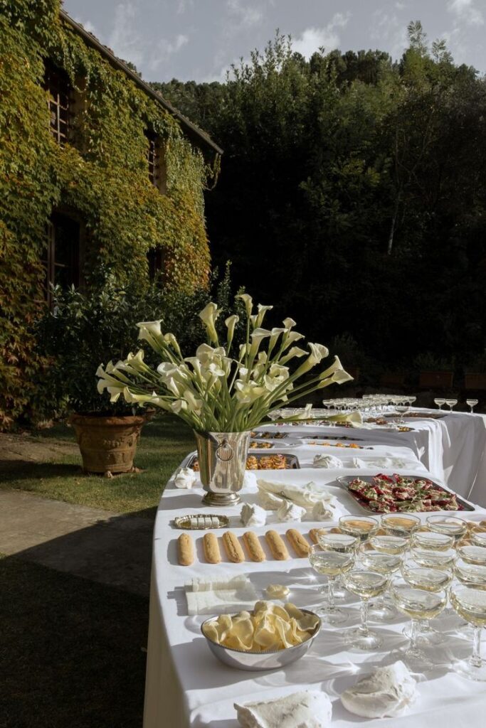 Outdoor buffet table with elegant calla lilies, assorted appetizers, and glasses of champagne, set in a lush garden setting.