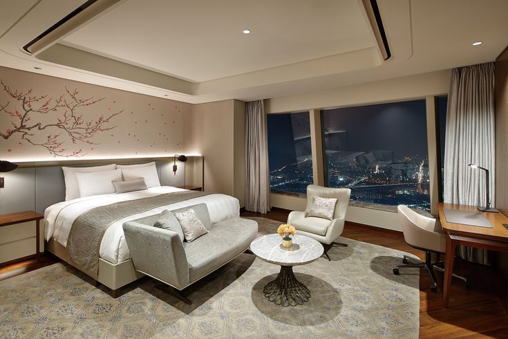 Luxurious hotel room with king-size bed, elegant decor, night city view through large window, and modern desk area.