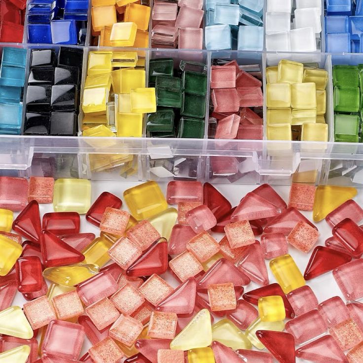 Colorful glass mosaic tiles in various shapes, sorted in compartments and scattered, perfect for artistic crafts.