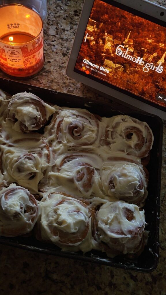 5121f700-78b3-4b50-b3b3-3a3b43d912f6 Cinnamon rolls with icing next to a lit candle and tablet playing a show on a cozy countertop. | Sky Rye Design Cinnamon rolls with icing next to a lit candle and tablet playing a show on a cozy countertop.