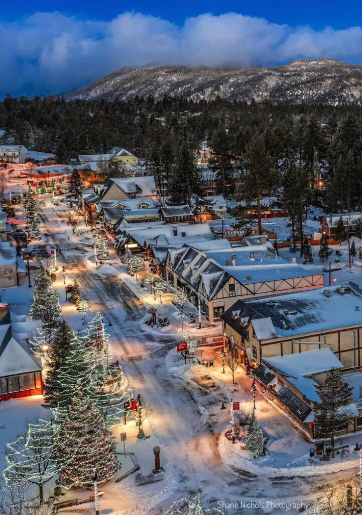 52c2bd01-18e1-41cc-b0b9-f5cd9a366117 Snow-covered town with festive lights and mountain backdrop at dusk. Cozy winter scenery with charming buildings. | Sky Rye Design Snow-covered town with festive lights and mountain backdrop at dusk. Cozy winter scenery with charming buildings.