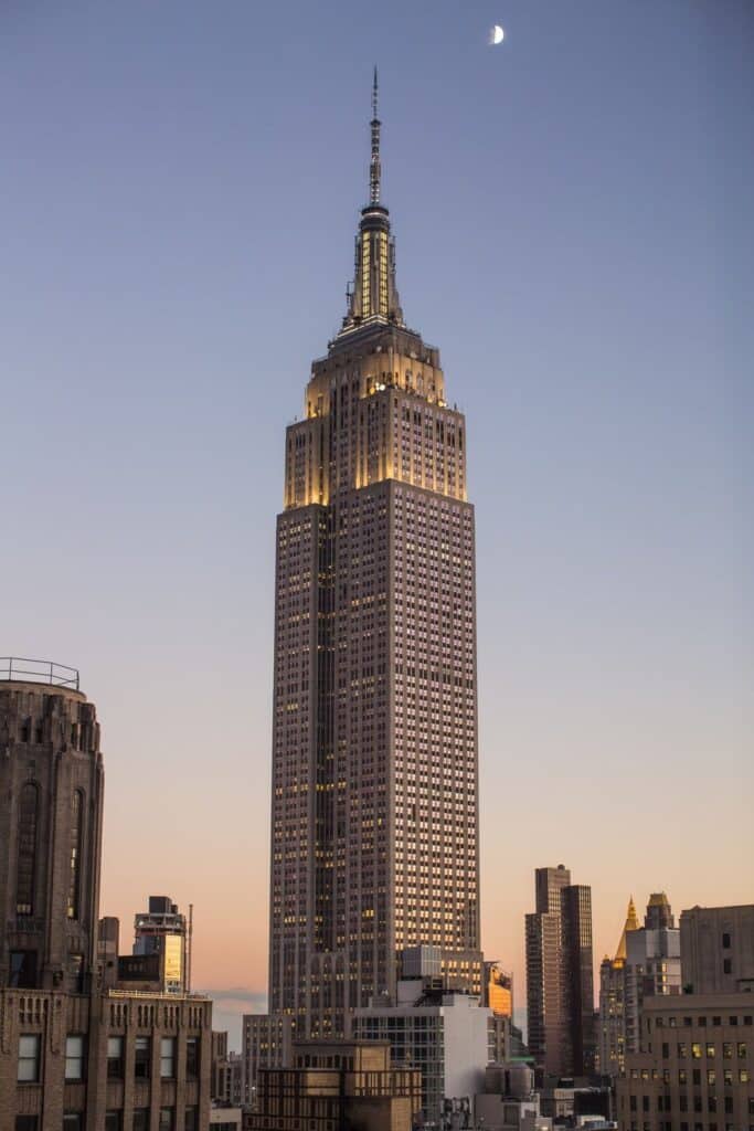 Empire State Building at sunset with a crescent moon, New York City skyline in the background.