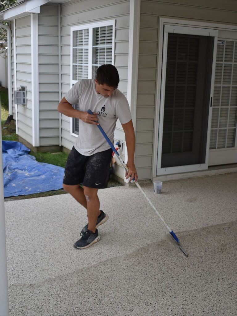 Man applying epoxy on a patio surface outside a grey house, enhancing durability and appearance.