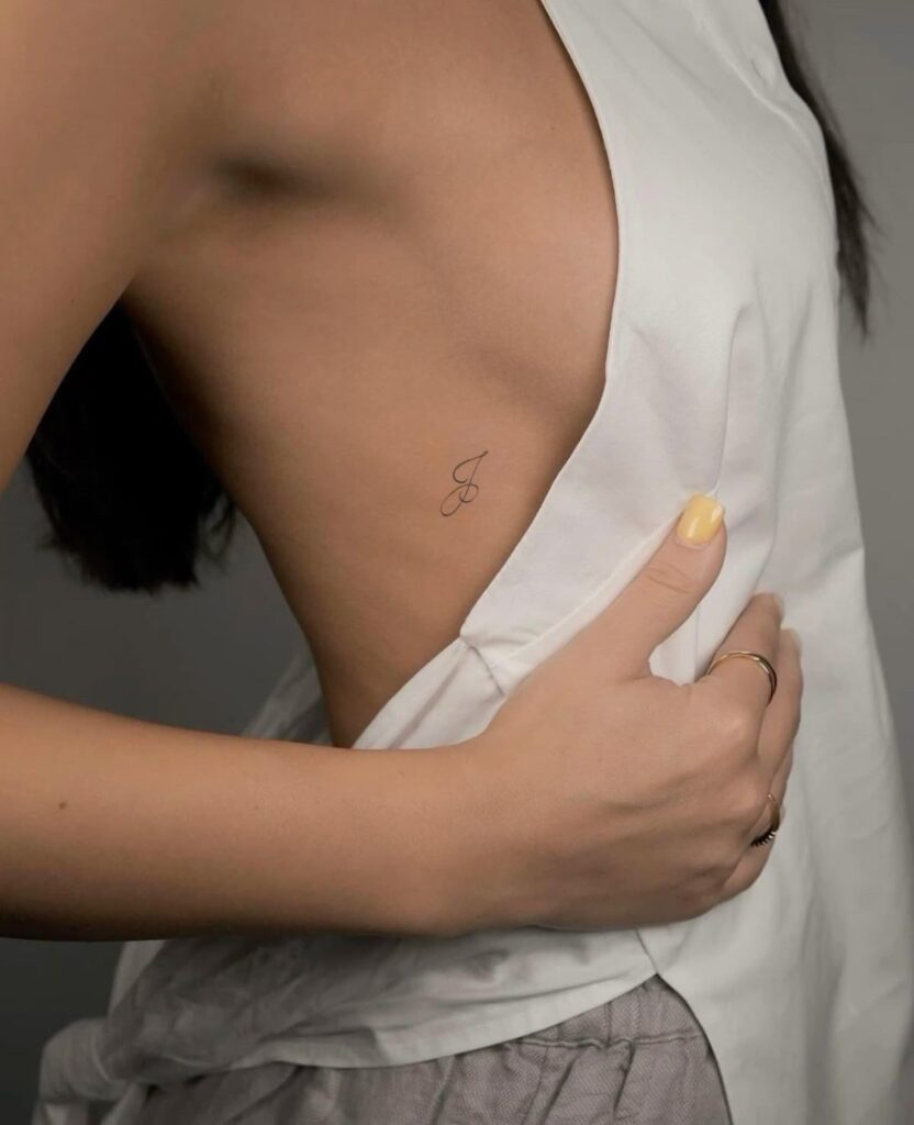 5badac092de07b825b928cacd5b35c21 Minimalist tattoo of the letter J on a woman's side under a white top, showcasing delicate design and placement. | Sky Rye Design Minimalist tattoo of the letter J on a woman's side under a white top, showcasing delicate design and placement.