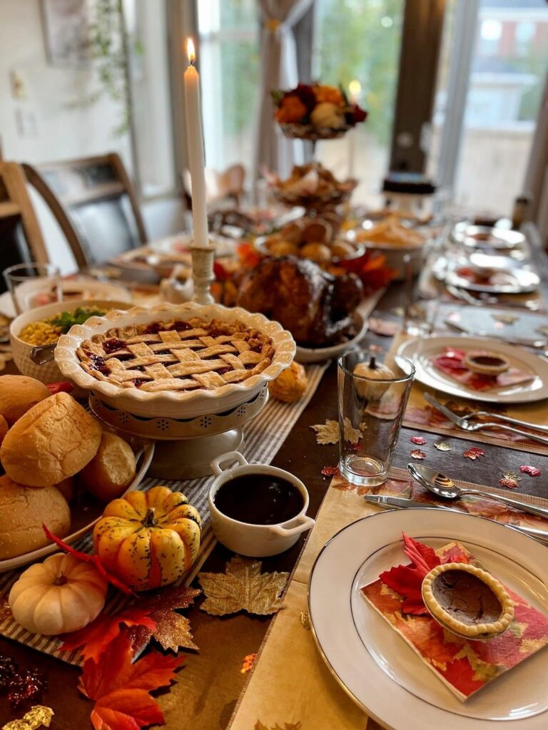 Festive Thanksgiving table with a pie, roasted turkey, lit candle, autumn leaves, and pumpkins for decor.