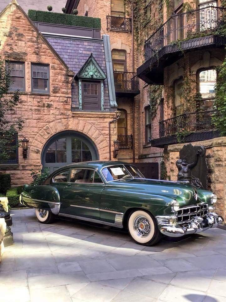 Vintage green car parked in front of an ivy-covered, historic stone building with classic architecture.