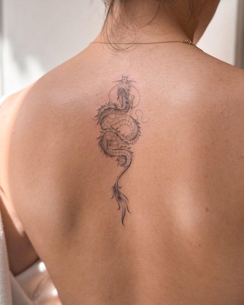 Detailed dragon tattoo on a person's upper back, showcasing intricate design and fine lines.