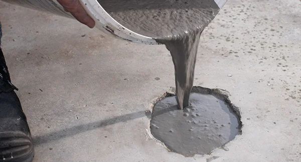 Pouring concrete mix into a hole in the floor for repair and leveling.