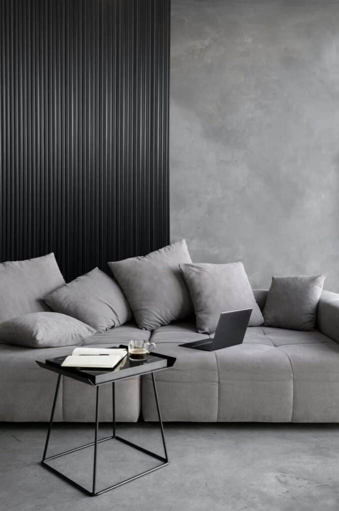 Modern grey living room with cozy sofa, laptop, and coffee on side table. Stylish interior design with textured walls.