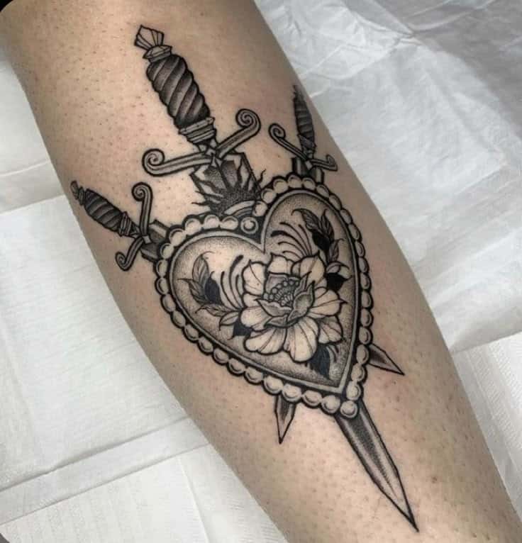 Detailed heart tattoo with a flower and three daggers on forearm. Black and gray ink.