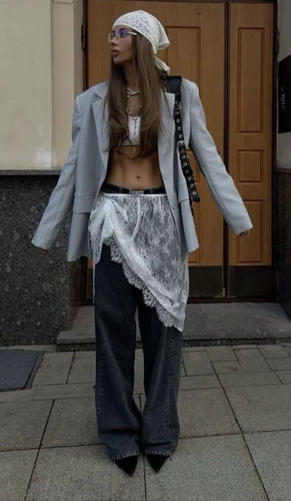 Fashionable woman in trendy layered outfit with lace skirt, blazer, and bandana posing outdoors. Urban street style.