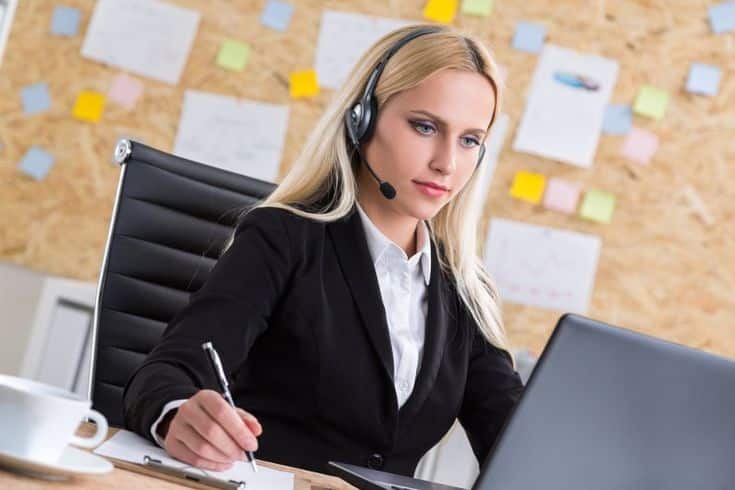 Businesswoman in a headset working at laptop with notes in office, focusing on customer service and communication.