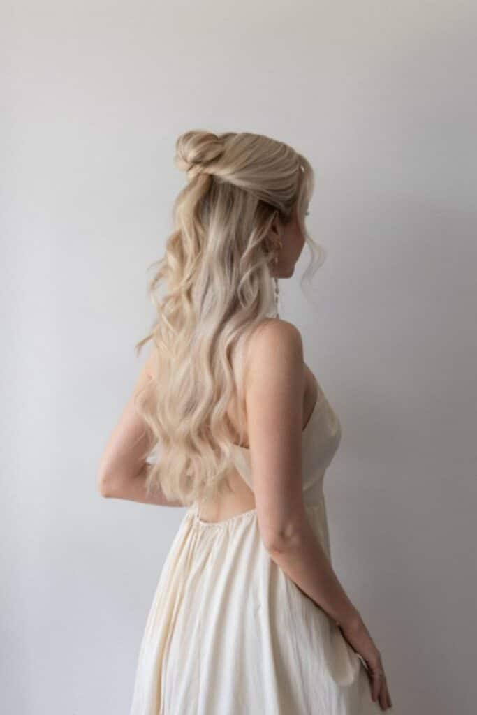 60 Second Half Up Half Down Hair Tutorial ❤️ Blonde woman with wavy half-up hairstyle in a white dress, facing away against a plain background. | Sky Rye Design Blonde woman with wavy half-up hairstyle in a white dress, facing away against a plain background.